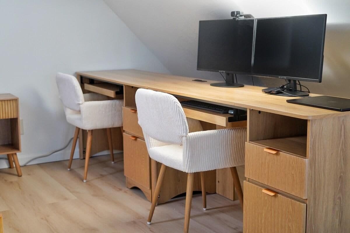 Um espaço de trabalho moderno com escrivaninha de madeira, duas cadeiras brancas e dois monitores.
