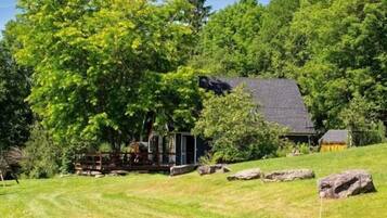 A cabin with a deck, surrounded by a grassy area and trees.