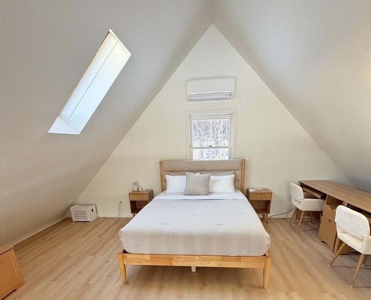 Un dormitorio con techo inclinado, una cama, un escritorio y una silla.