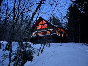 A cabin with a large window and a deck, surrounded by trees and snow. - Modern Lakeside Retreat on 5.6 Upstate Acres (Delancey)