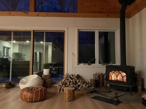 Ein gemütliches Wohnzimmer mit Kaminofen, einem großen Glastür, das auf einen Balkon führt, und einer modernen Küche, die durch das Glas sichtbar ist.