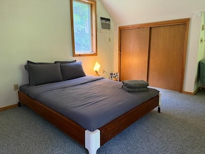 Ein Schlafzimmer mit Bett, Fenster, Kleiderschrank und Nachttisch mit Lampe.
