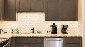 A kitchen with dark cabinets, a stainless steel dishwasher, a coffee maker, and a patterned backsplash.