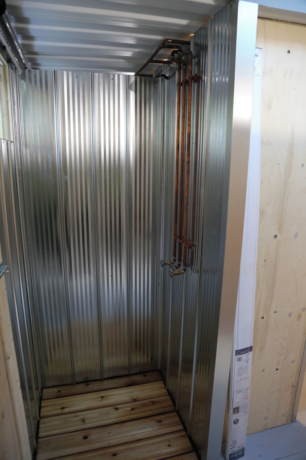 Ein Zimmer mit Wänden aus Metall, Holzboden, einer Tür mit Griff und einer sichtbaren Rohrleitung.