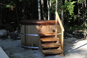 A hot tub with a wooden exterior and a wooden bench with steps leading up to it, surrounded by trees. - Ash, the tiny cabin in the woods (Markdale)