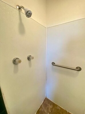 A corner of a bathroom with a shower, a grab bar, and a towel rack.