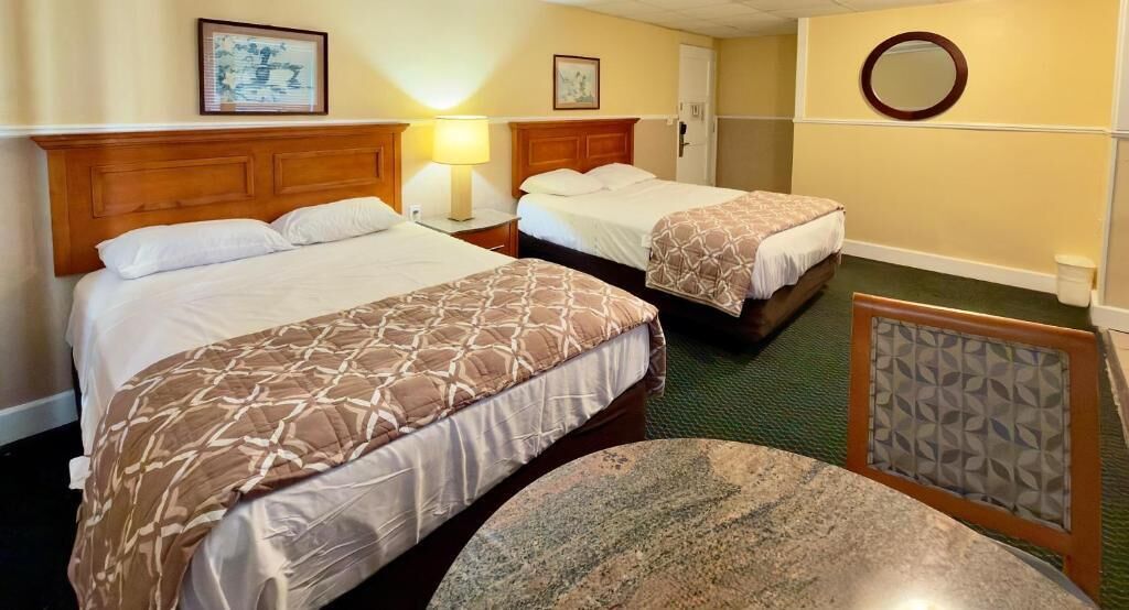 A hotel room with two beds, a round table, and a mirror.