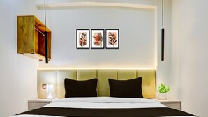 A modern hotel room with a bed, bedside tables, a nightstand, a wall-mounted light, and three framed leaf artworks. - Super Collection O George Town (Prayagraj)