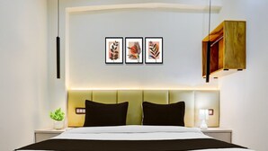 A hotel room with a bed, two bedside tables, a bedside lamp, a small plant, and three framed leaf artworks on the wall. - Super Collection O George Town (Prayagraj)