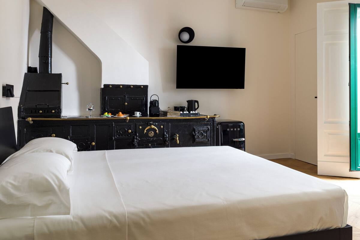 Un dormitorio con una cama, un aparador negro, un televisor de pantalla plana y piso de madera.