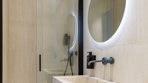 Un baño moderno con cabina de ducha de vidrio, lavamanos integrado, un espejo redondo y un perchero.