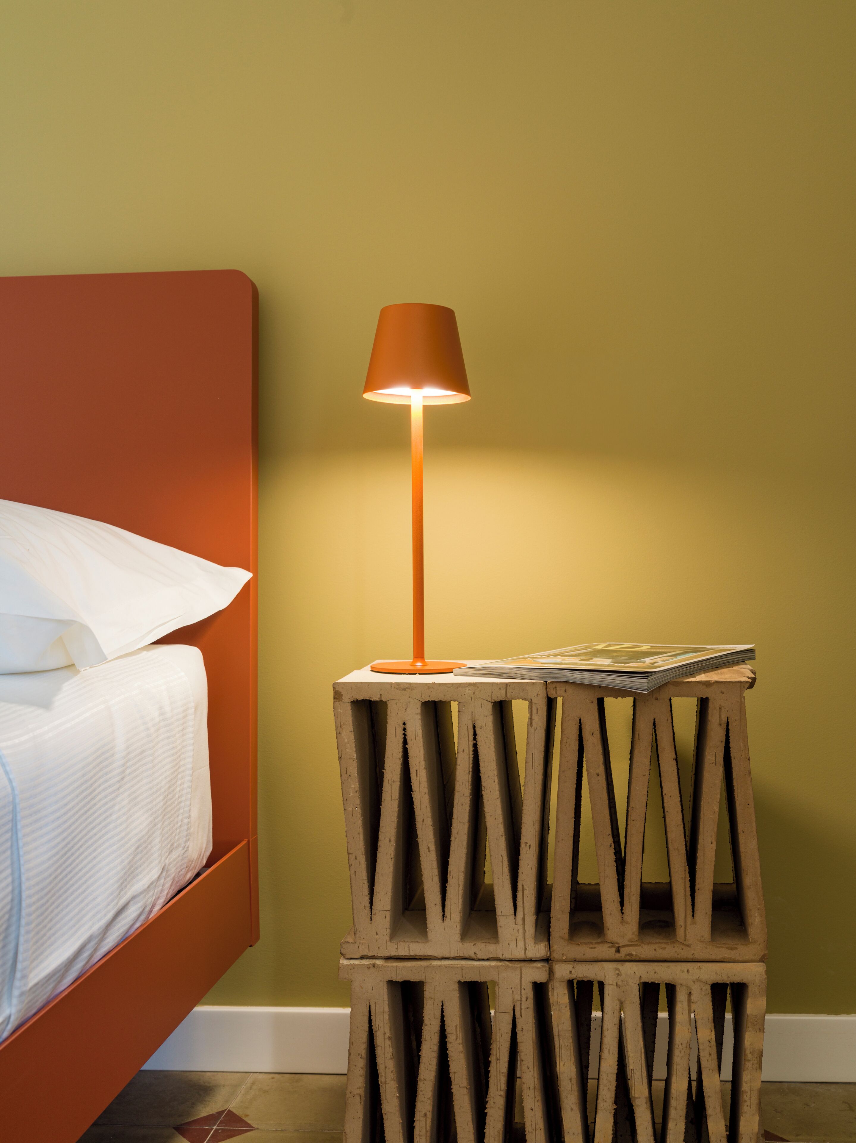 Un letto con lenzuola bianche, un comodino in legno con una lampada e una parete verde.