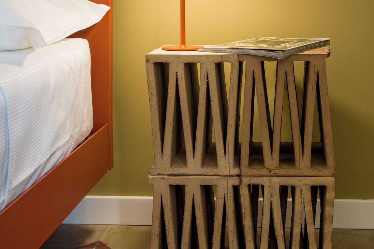 Una cama con sábanas blancas, una mesita de noche de madera con una lámpara, y una pared verde.