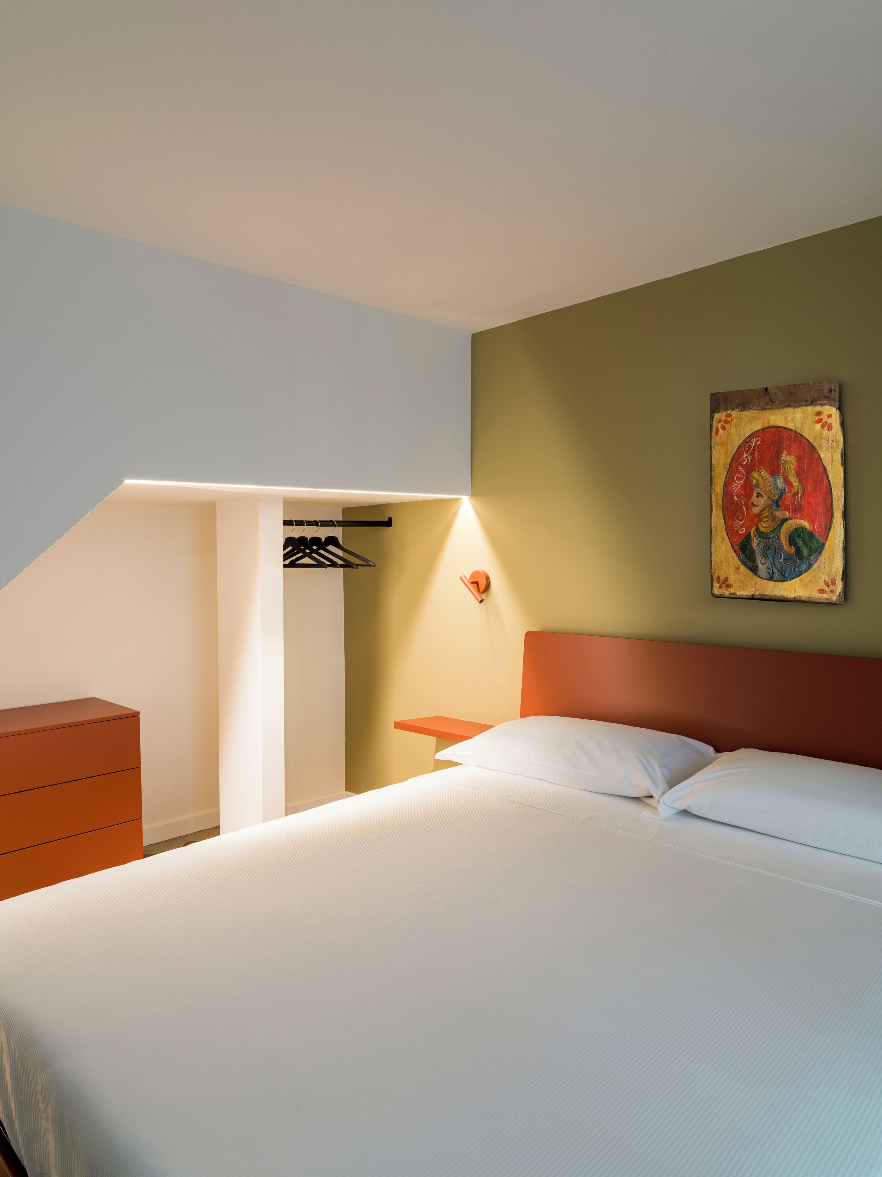 Camera da letto con un letto, una cassettiera, un comodino e una lampada a parete.