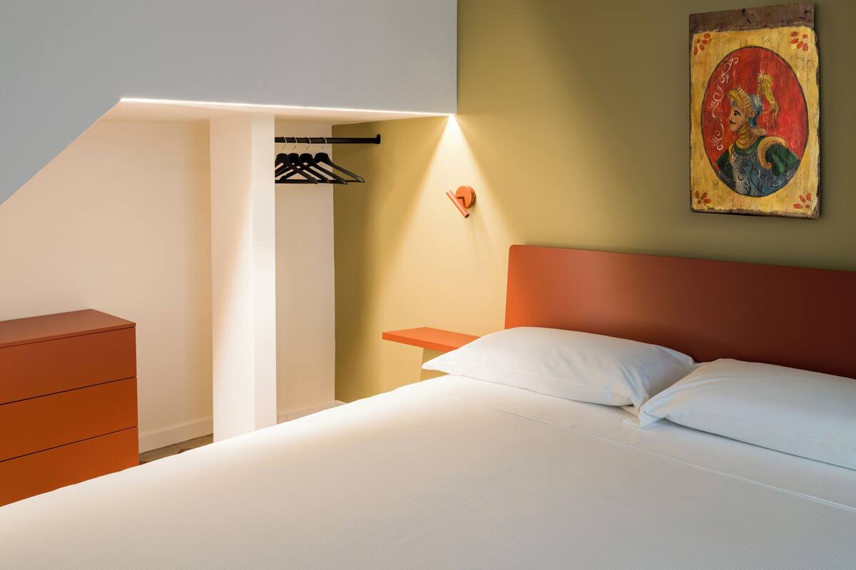 Un dormitorio con cama, cómoda, mesita de noche y lámpara de pared.