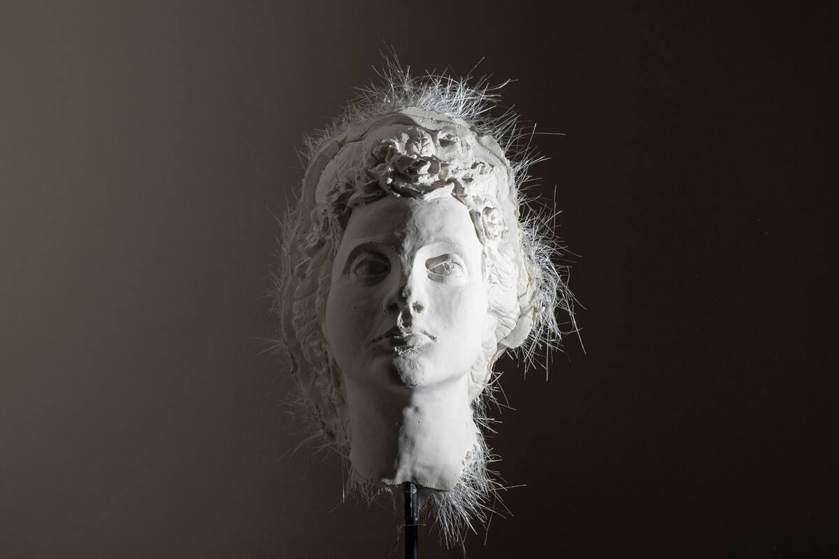 Una escultura de busto sobre un pedestal frente a una pared oscura.