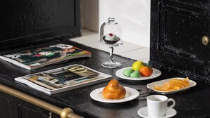 Una mesa de madera negra con una campana de vidrio que contiene un postre, un plato con pasteles, una taza y una revista.