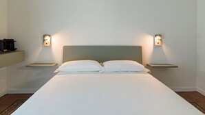 Una cama bien hecha con dos almohadas, cabecera y dos mesitas de noche con lámparas de pared.