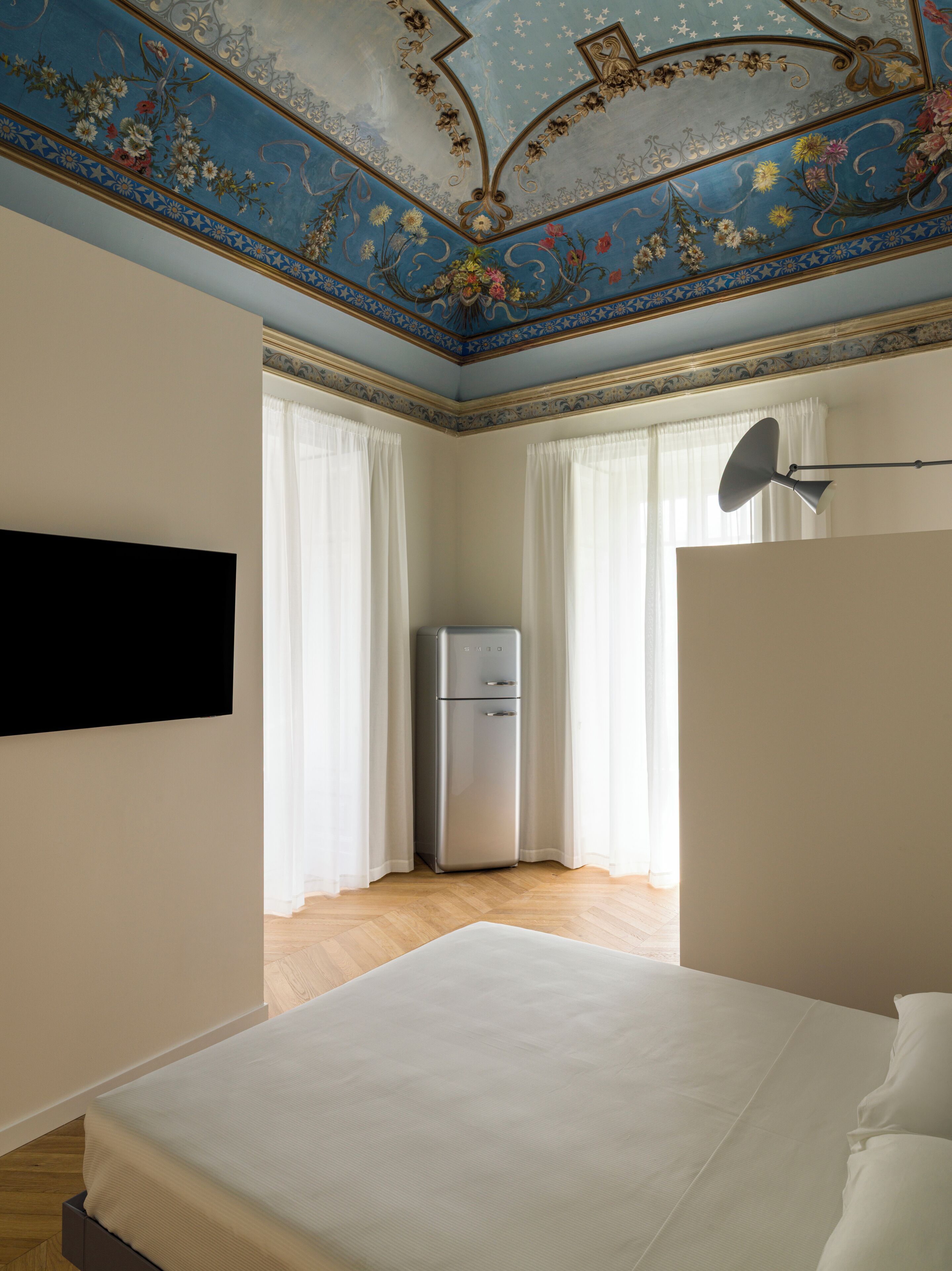 Una camera da letto con un letto, una TV a muro, un frigorifero e un soffitto decorato con motivi floreali e a stelle.