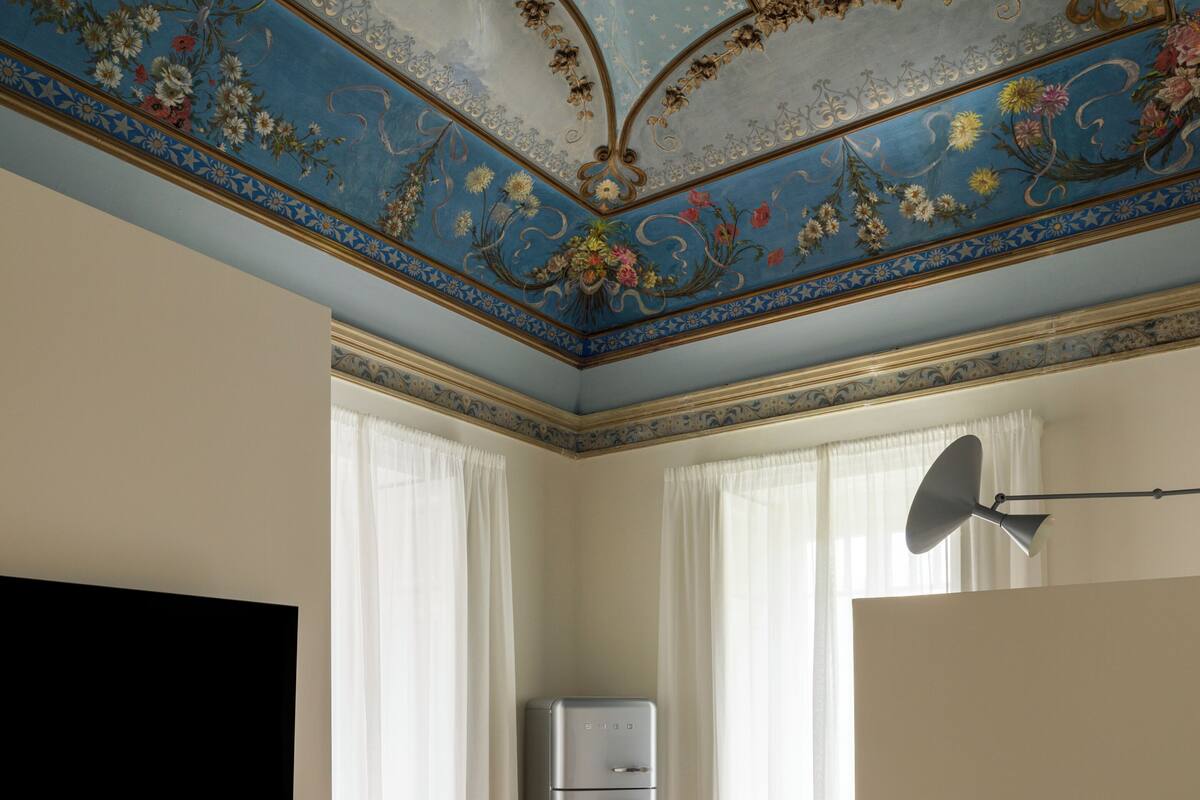 Un dormitorio con cama, televisor de pared, refrigerador y techo con motivos florales y de estrellas.