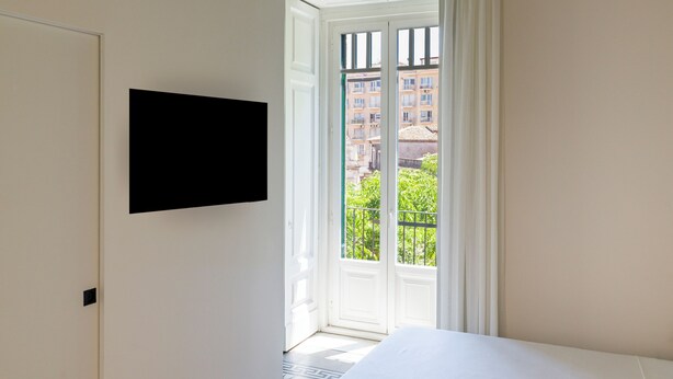 Un dormitorio con una cama, un televisor montado en la pared y vistas al exterior a través de una puerta.