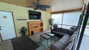 Eine überdachte Terrasse mit Deckenventilator, einer hölzernen Bank, einer Couch und einem an der Wand montierten Fernseher.