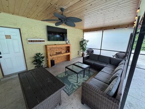 A covered patio with a ceiling fan, a wooden bench, a sofa, and a television mounted on the wall. - Updated 3-bedroom POOL house with AC in gorgeous Fort Myers (Fort Myers)