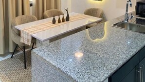 Una cocina moderna con encimera de granito, luces colgantes, una mesa de comedor y horno empotrado.