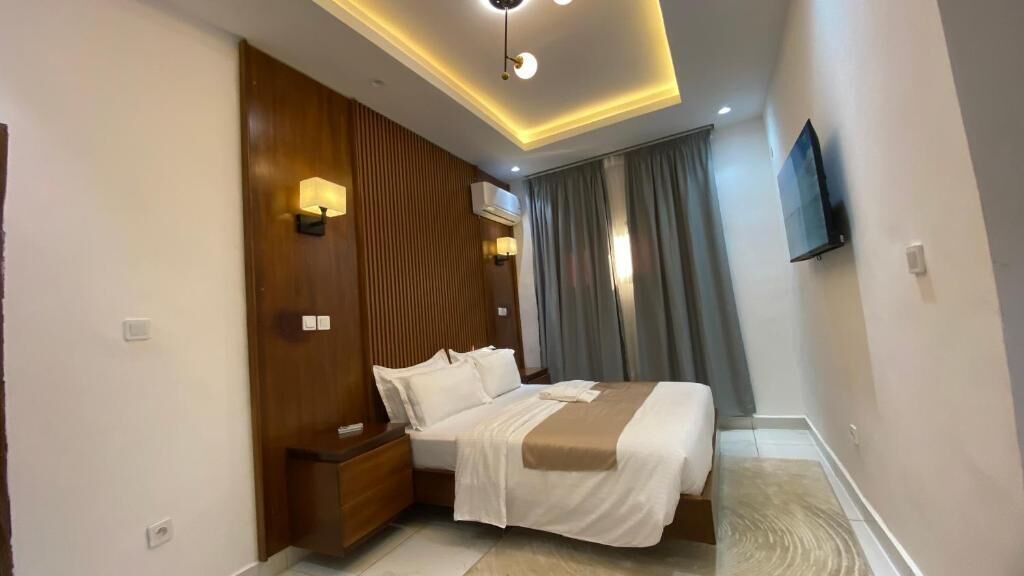 A hotel room with a bed, bedside tables, a wall-mounted TV, and a ceiling light fixture.