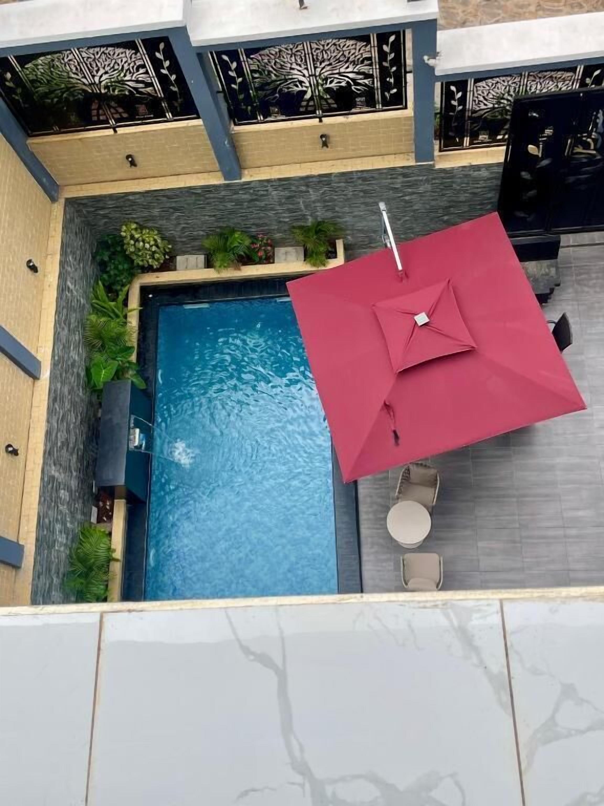 An aerial view of a rooftop pool area with a red umbrella, seating, and potted plants.