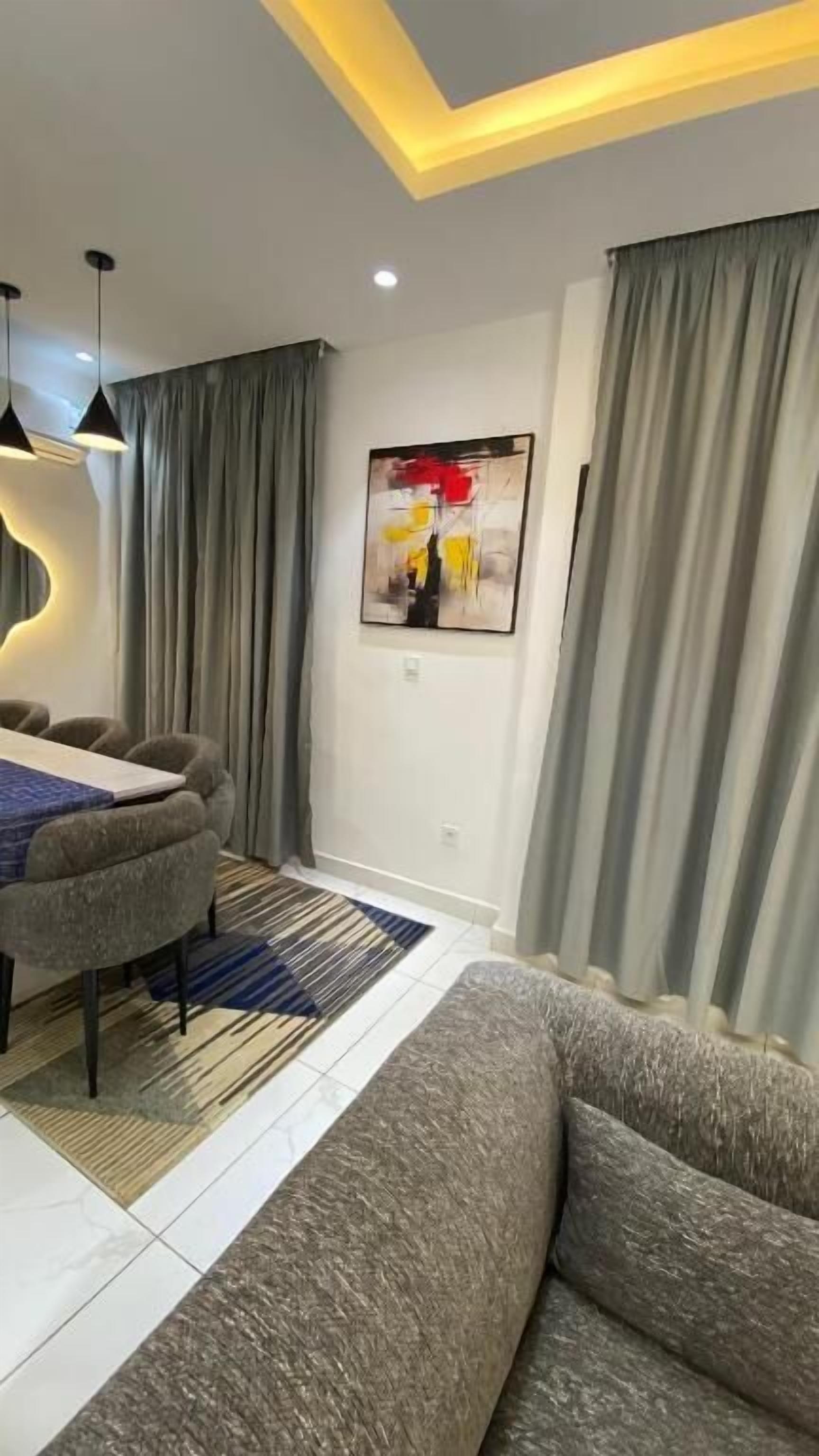 A modern living room with a sofa, a dining table with chairs, a painting on the wall, and grey curtains.
