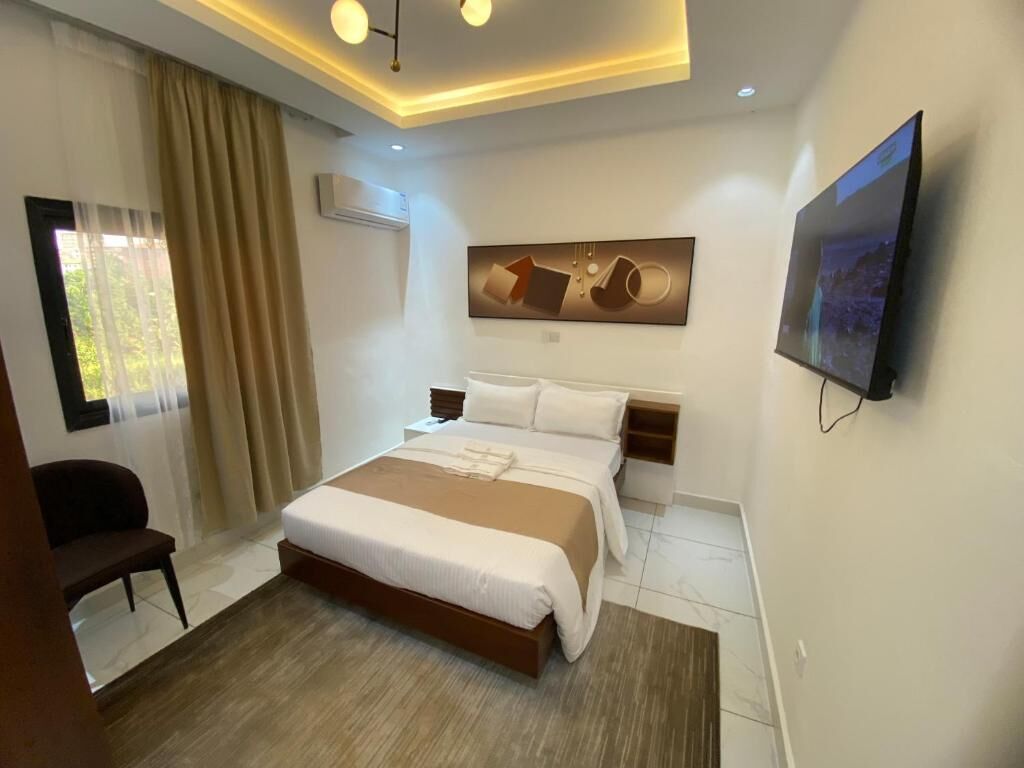 Een moderne hotelkamer met een groot bed, een flatscreen televisie, een schilderij aan de muur en een raam met gordijnen.