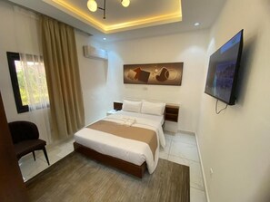 A modern hotel room with a large bed, a flat-screen TV, a painting on the wall, and a window with curtains. - AJ3 LUXURY HOME (Yaoundé)