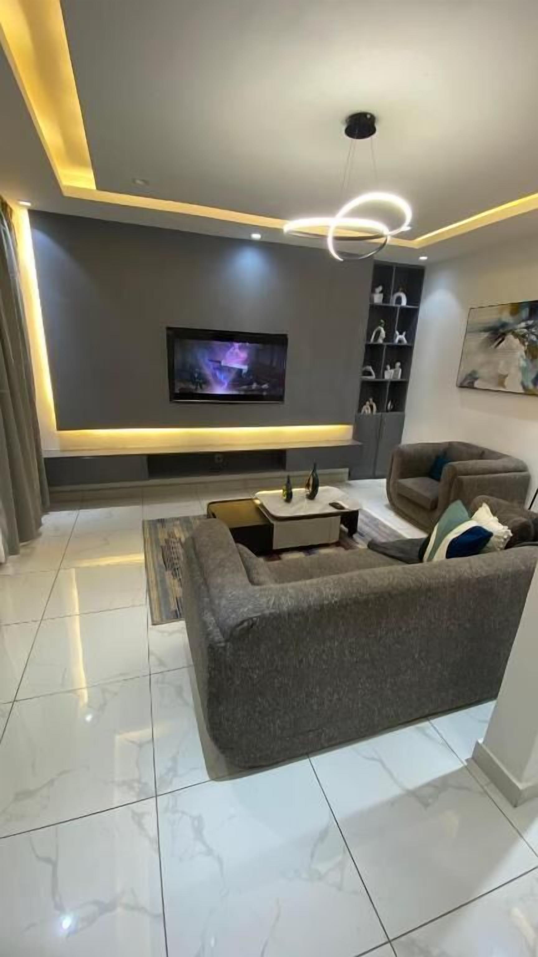 A modern living room with a flat-screen TV, a sofa, a coffee table, and a pendant light.