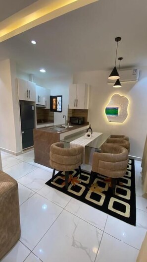 A modern kitchen with white cabinets, a central island, and a dining area with two chairs. - AJ3 LUXURY HOME (Yaoundé)