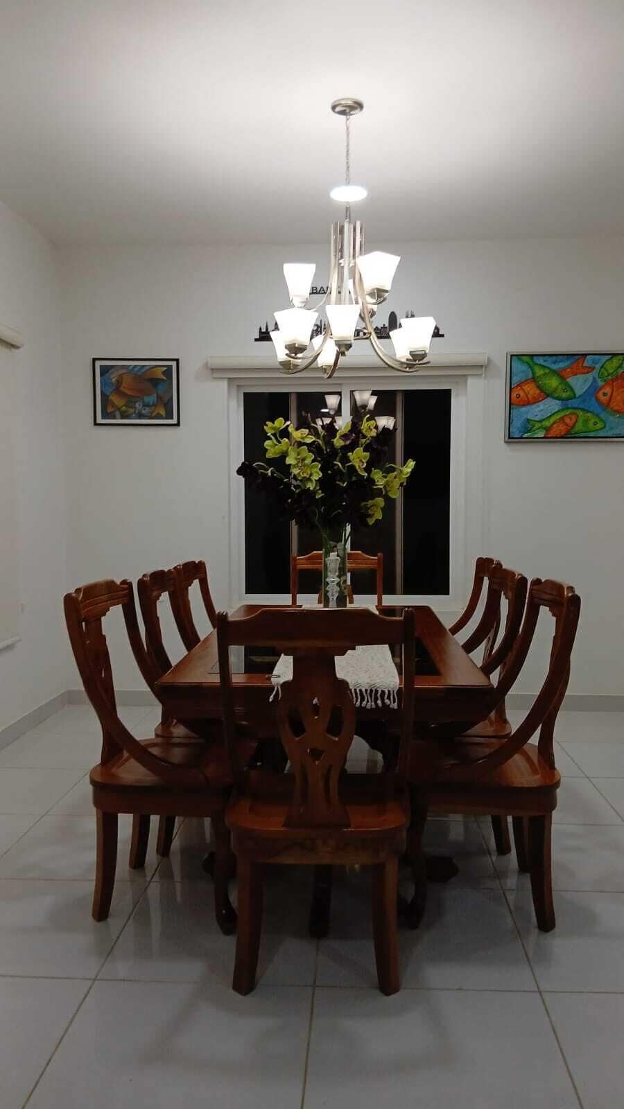 Een eetruimte met een kroonluchter, houten stoelen, een tafel en kunstwerken aan de wanden.