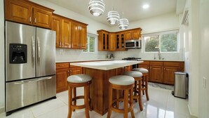 Una cocina moderna con armarios de madera, electrodomésticos de acero inoxidable, una isla central con taburetes e iluminación colgante.
