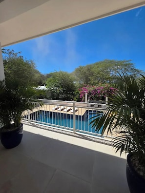Un balcon avec une piscine, entouré de plantes en pot et d’arbres.
