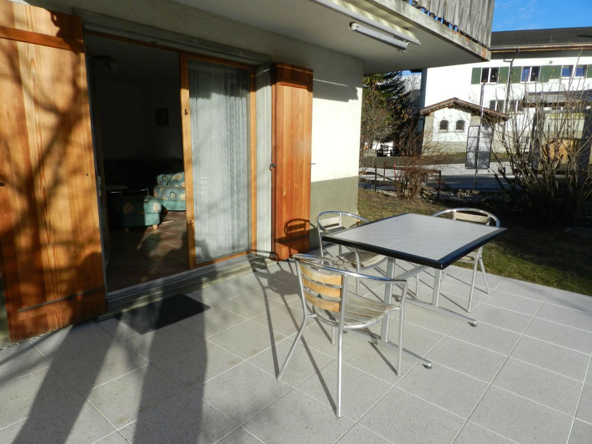 An outdoor patio with a table and chairs, a sliding glass door, and a view of a building in the background.