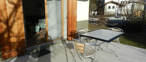 An outdoor patio with a table and chairs, a sliding glass door, and a view of a building in the background.