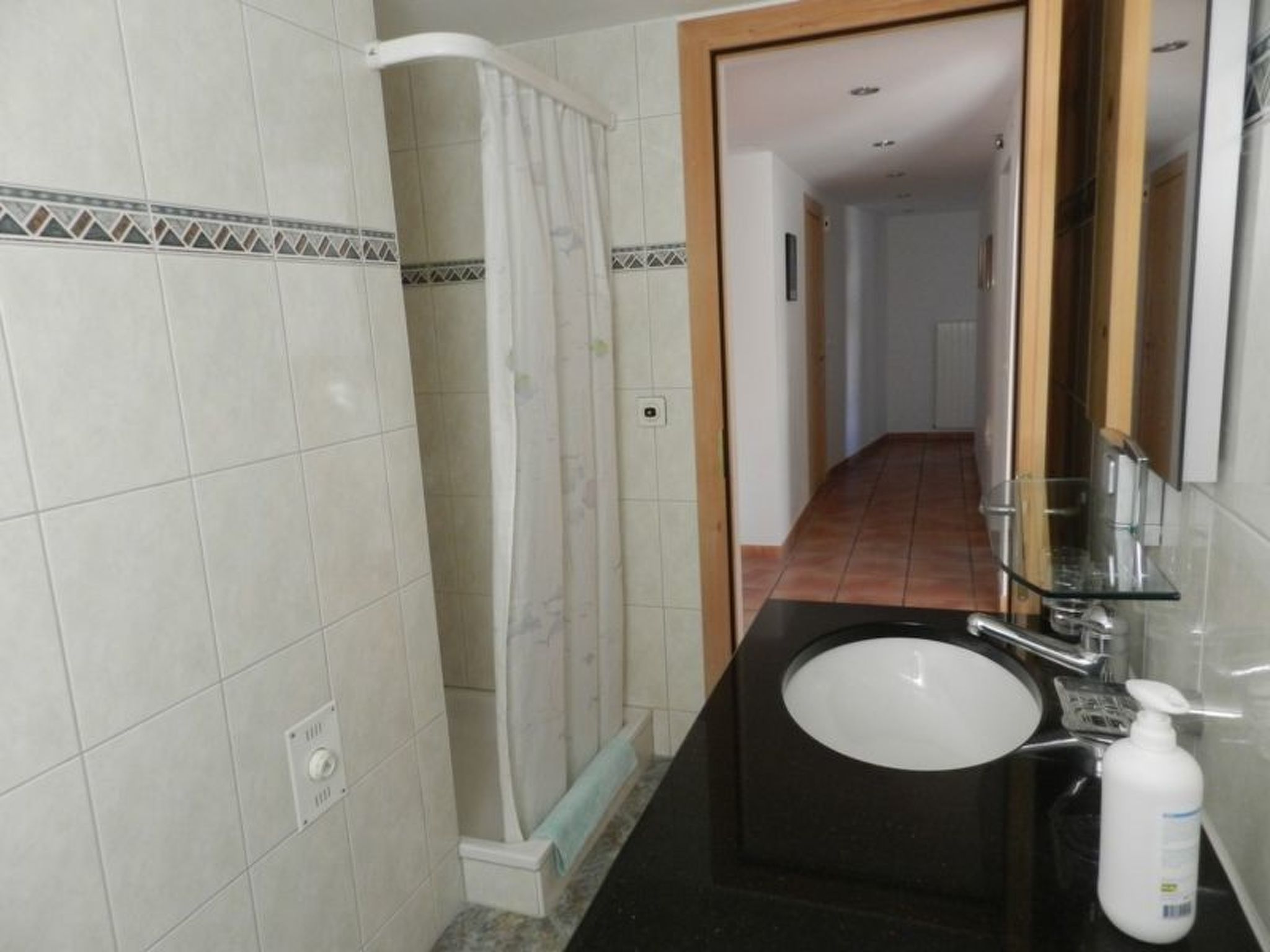 Ein Badezimmer mit Waschbecken, Spiegel, Duschvorhang und Fliesenwänden.