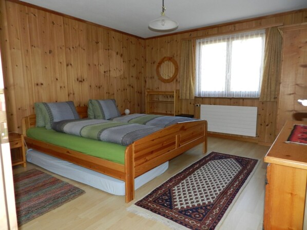 A wooden-paneled room with a bed, a small table, a radiator, and a window with curtains. - Zignaus Demont, Vella, (Vella), 44015B by Interhome (Vella)