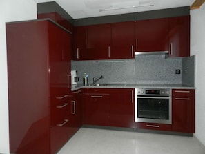 A kitchen with red cabinets, a stainless steel oven, and a granite countertop. - Zignaus Demont, Vella, (Vella), 44015B by Interhome (Vella)