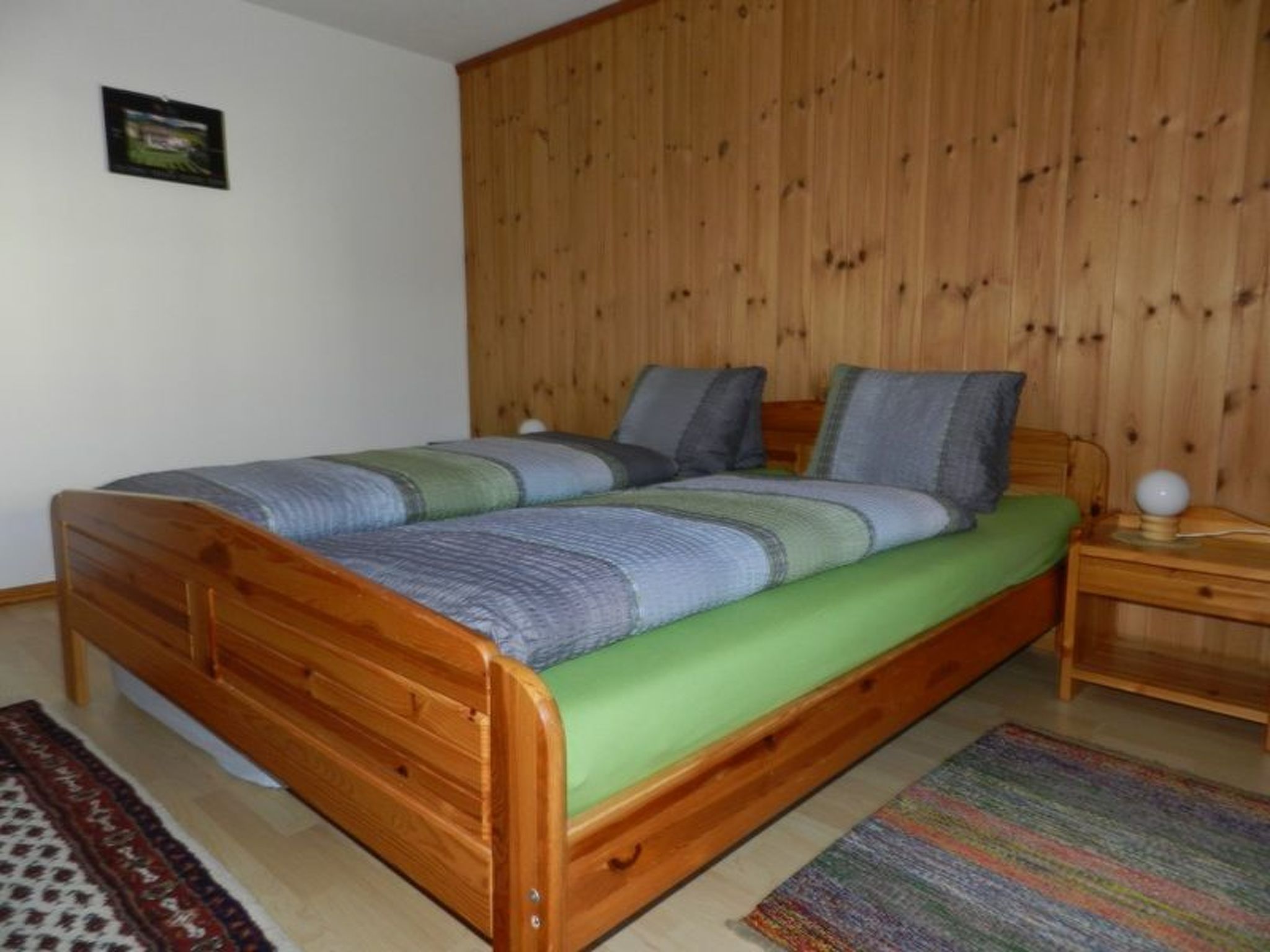 Camera singola con un letto matrimoniale, una testiera in legno, un materasso verde e un comodino con una lampada.