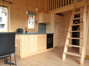 Interior de una cabaña de madera con una cocina, una mesa de comedor y una escalera de madera.