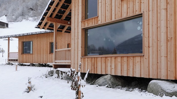 A wooden cabin with large windows, a balcony, and a snowy landscape.