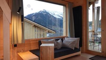 Ein modernes Interieur mit Holzboden, einer Couch mit Kissen, einer Holzbank und einem großen Fenster mit Blick auf die Berge.