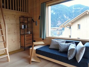 Eine Holzhütte mit einem Bett, einem Bücherregal und einem Fenster mit Blick auf die Berge.