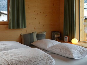 Una habitación acogedora con paredes de madera, dos camas con ropa blanca, una mesita de noche con lámpara y una ventana con cortinas.