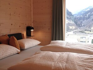 A hotel room with wooden walls, a bed with white bedding, a nightstand with a lamp, and a window with a mountain view.